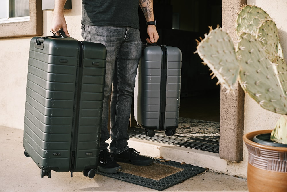 Mann in schwarzer Jeans und schwarzen Lederschuhen neben schwarzer Gepäcktasche