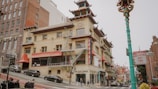A vibrant street scene in a Chinatown district featuring a building with traditional Chinese architectural elements, including pagoda-style roofs and intricate decorations. The street is bustling with pedestrians and vehicles. Brightly colored signs and lanterns add to the cultural atmosphere.