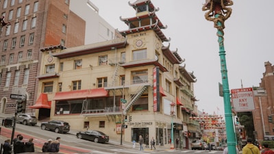 A vibrant street scene in a Chinatown district featuring a building with traditional Chinese architectural elements, including pagoda-style roofs and intricate decorations. The street is bustling with pedestrians and vehicles. Brightly colored signs and lanterns add to the cultural atmosphere.