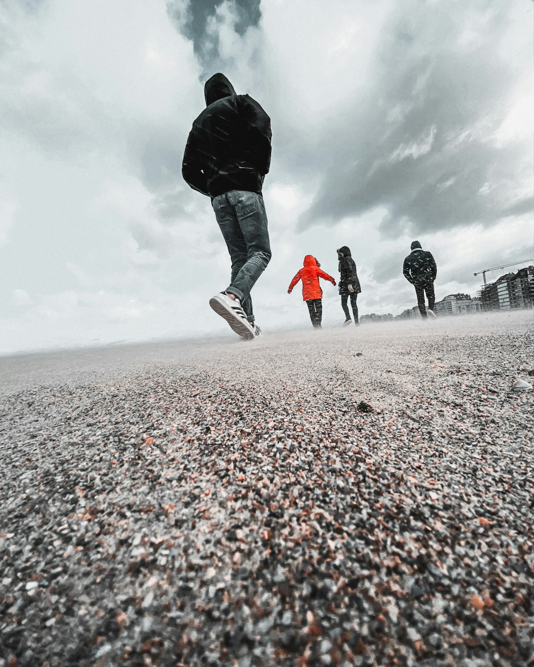 man in black jacket and blue denim jeans walking on gray sand during daytime