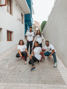 A group of young creators wearing different styles of print-on-demand tees, laughing and hanging out in a neon-lit alley.