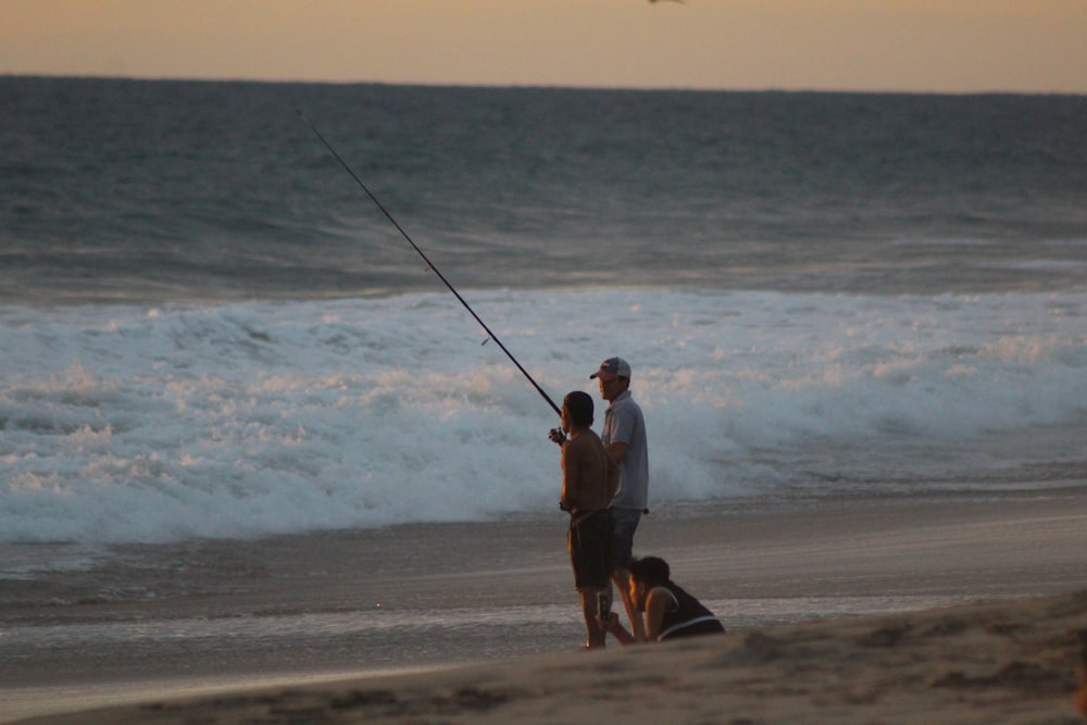 man and woman holding fishing rods walking on beach during daytime