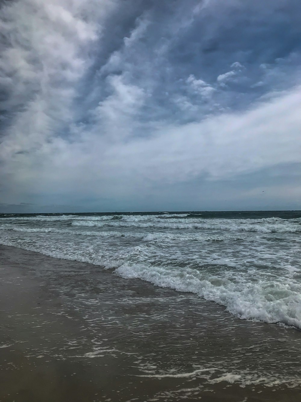 昼間の青と白の曇り空の下、海岸に打ち寄せる波