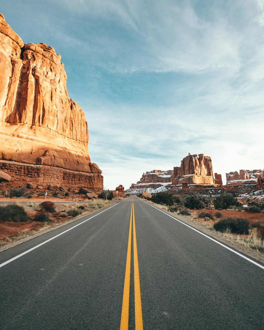 gray asphalt road between brown rock formation under blue and white sunny cloudy sky during daytime