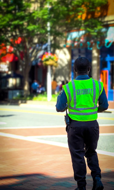 A confident security officer in uniform standing alert near an industrial estate entrance.