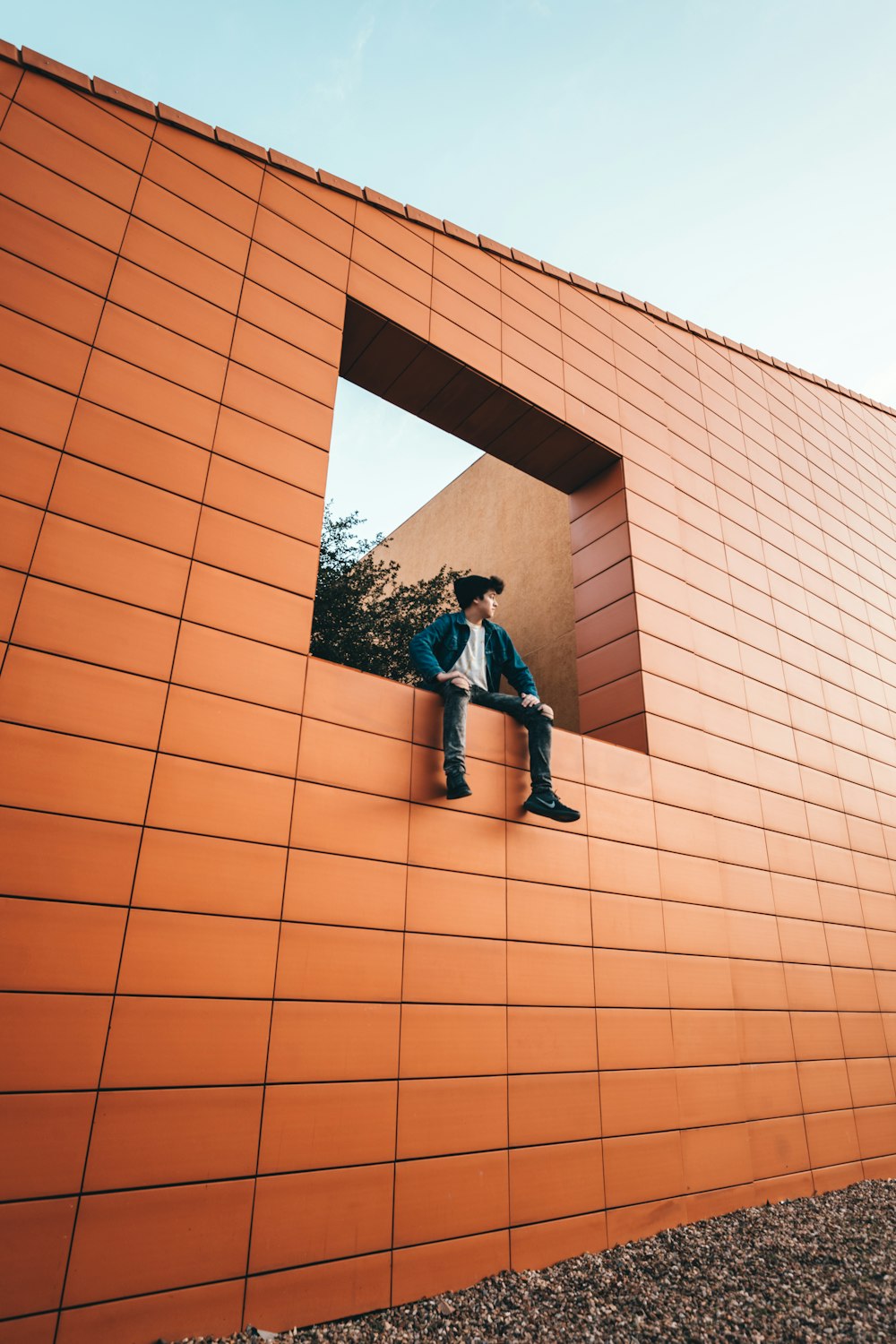 man in black jacket and blue denim jeans standing beside brown concrete building during daytime