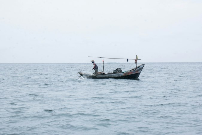 A fisherman standing in a small wooden boat on a calm grey sea
