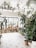 A bright and airy indoor garden space with an abundance of potted plants scattered throughout. The room features a high ceiling with additional plants placed on a balcony shelf above. Large windows allow natural light to flood the area, enhancing the lush green hues of the plants. Various ceramic pots and planters are neatly arranged, creating an organized and inviting atmosphere.