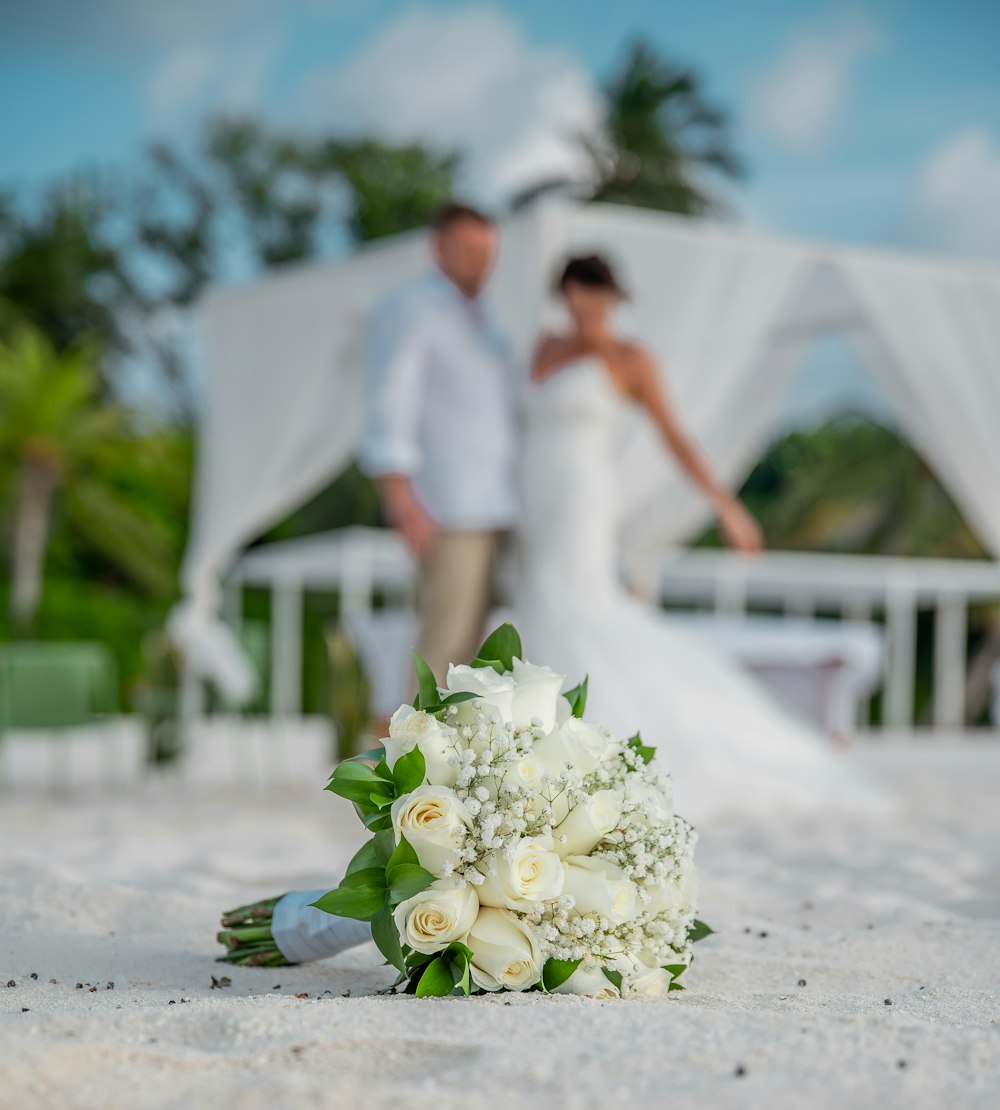 man in white dress shirt and woman in white dress holding bouquet of white roses