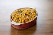 A ceramic dish filled with a serving of pasta, likely fettuccine, covered in a creamy sauce with visible herbs. The pasta is neatly arranged in the oval dish, which has handles on both ends.