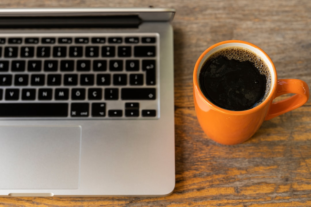 black coffee in orange ceramic mug beside macbook pro
