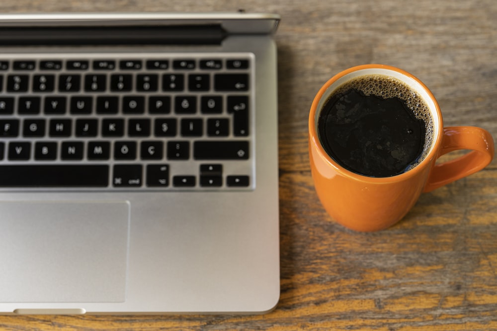 black coffee in orange ceramic mug beside macbook pro