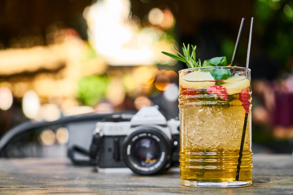 black and silver dslr camera beside clear drinking glass with yellow liquid