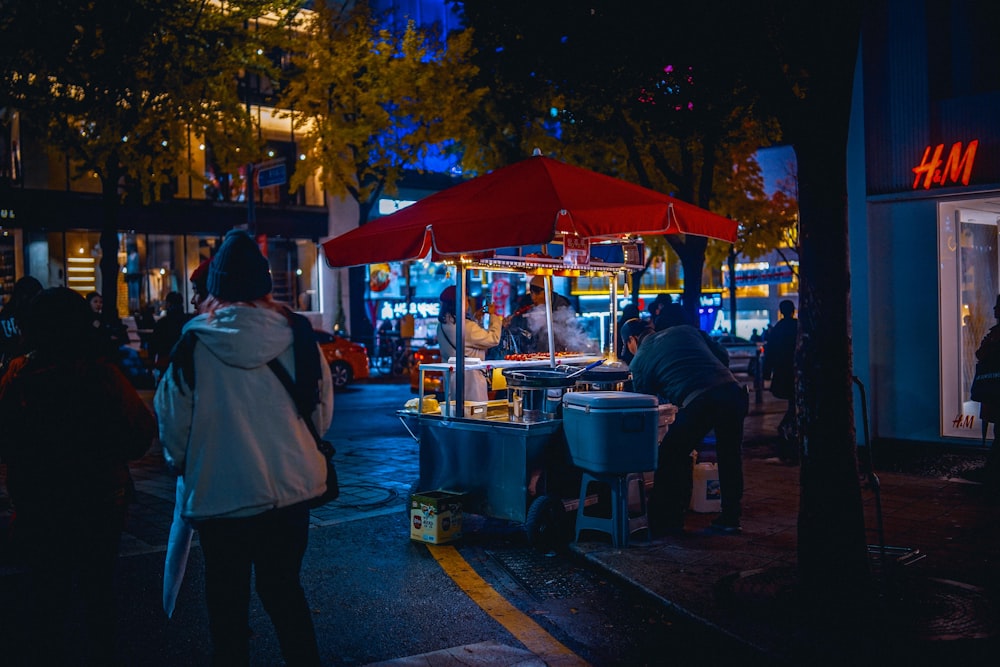 woman in pink jacket standing near red umbrella during night time