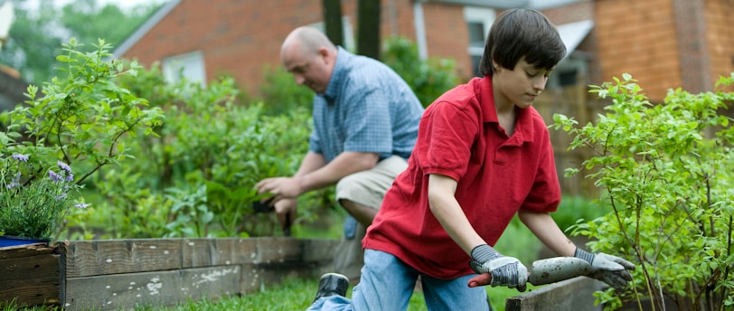 man in red polo shirt and blue denim jeans sitting on brown wooden bench during daytime