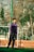 A young person stands on a sports field, wearing a purple and black tracksuit. The background features a wire fence and bare trees, suggesting an outdoor urban environment in a cooler season.
