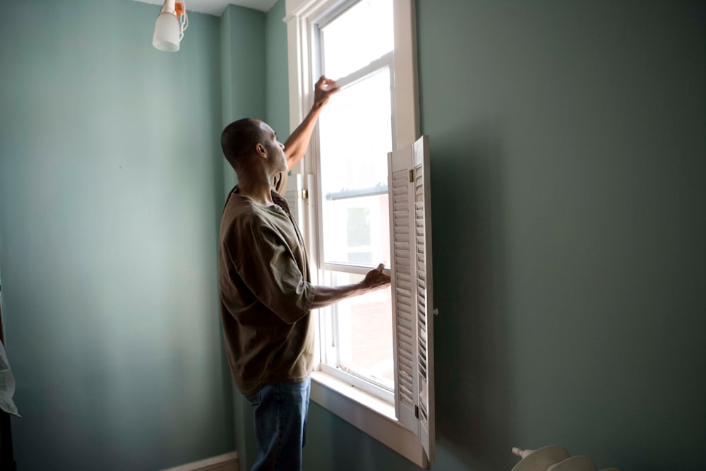 man in brown shirt and blue denim jeans standing near window