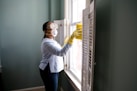 woman in white long sleeve shirt and blue denim jeans standing beside white wooden framed glass