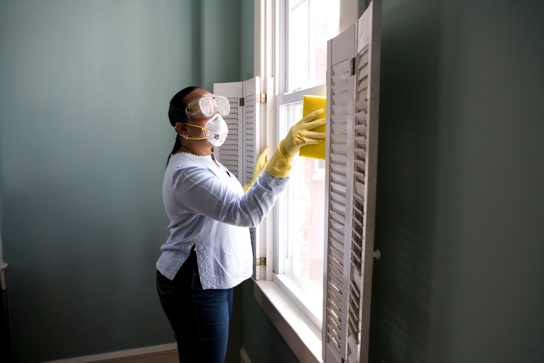 A woman, wearing a mask and gloves, deeply cleans a window.