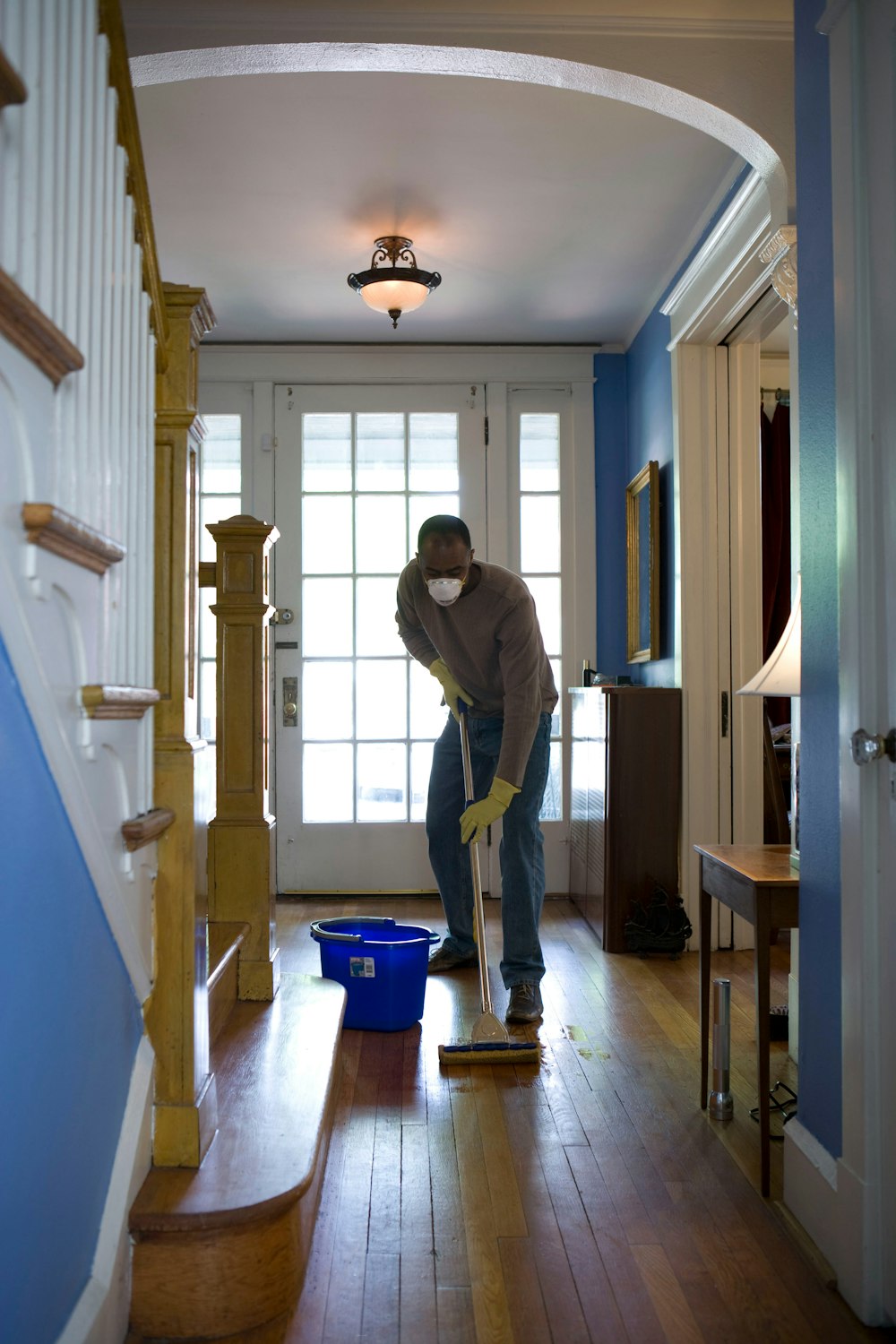 uomo in felpa con cappuccio grigia e jeans blu in piedi su parquet di legno marrone