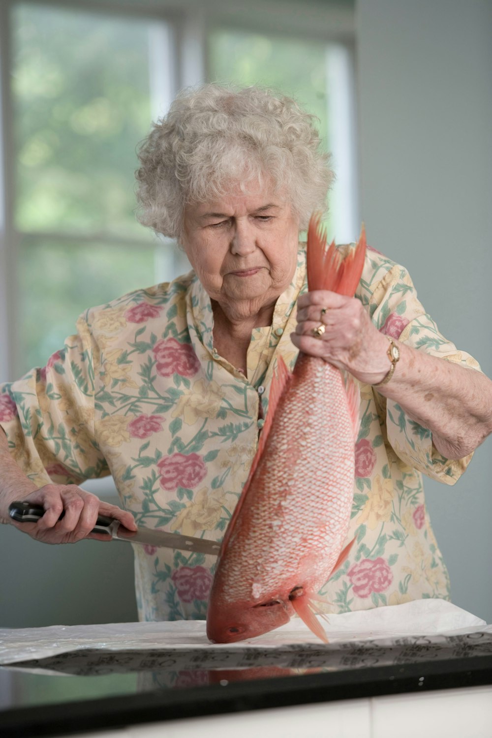 woman in yellow and pink floral shit holding a fresh fish 