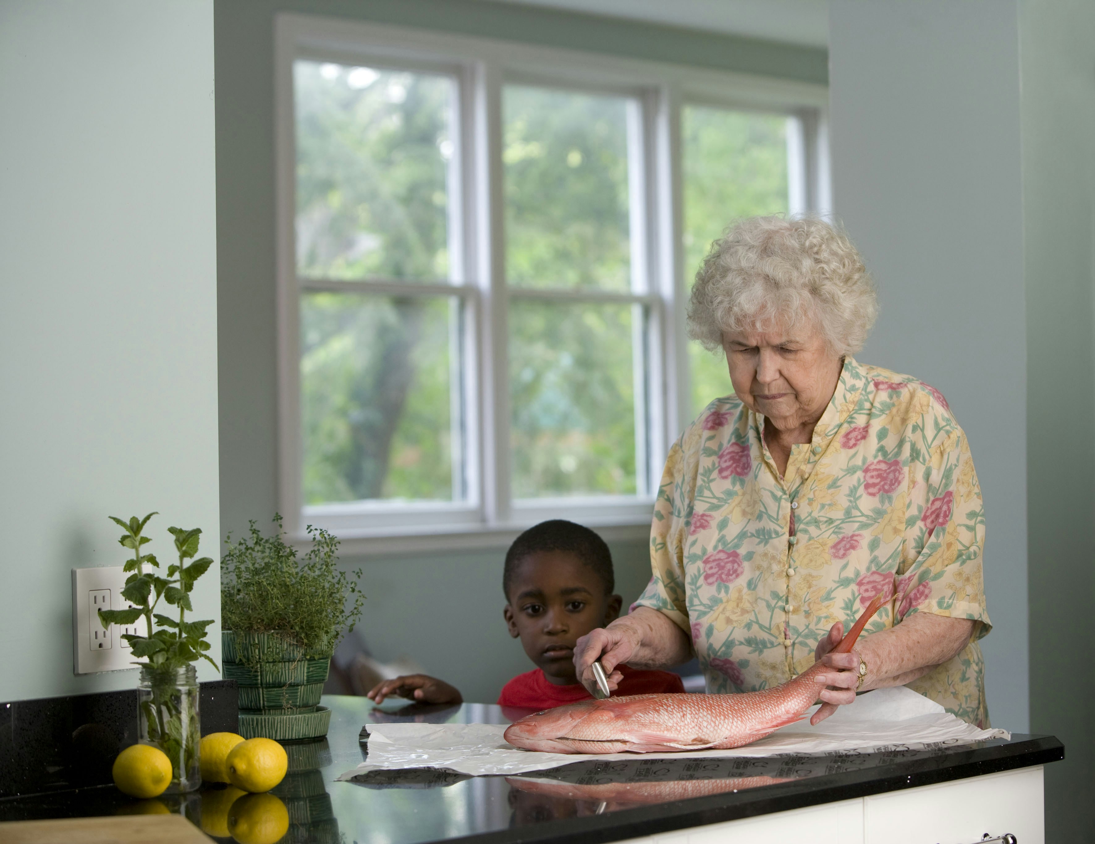 This elderly woman was in the process of preparing a fresh fish on her clean kitchen counter, while a young African-American boy watched. Teaching this youngster how to carefully process fresh fish is an important skill he will hopefully put to good use as he grows up.