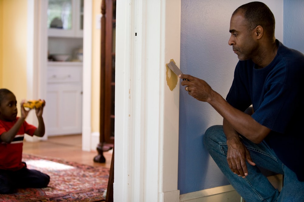 man in black crew neck t-shirt and blue denim jeans sitting on white wooden door