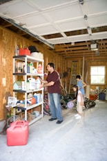 man in black t-shirt and blue denim jeans standing beside brown wooden shelf