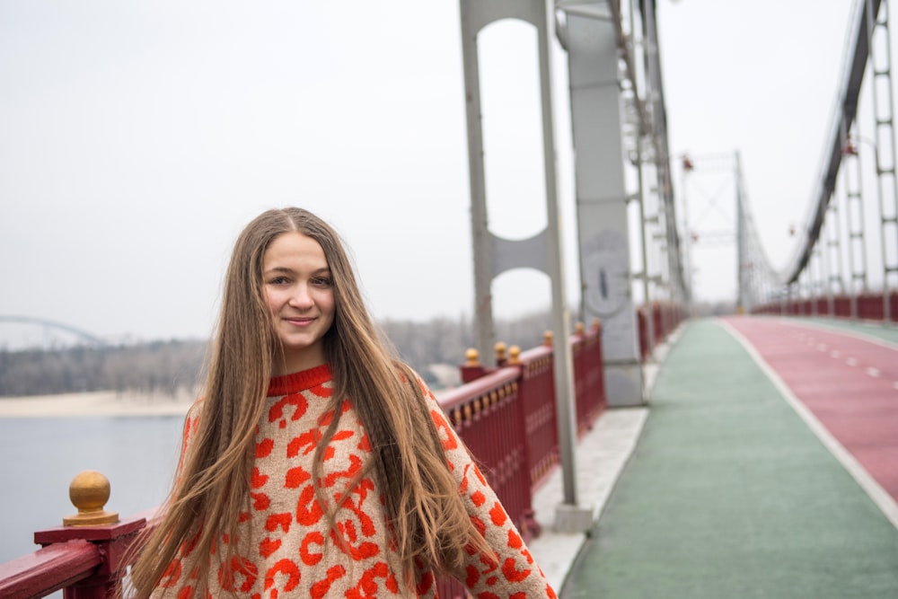 woman in red and white floral long sleeve shirt standing on bridge during daytime