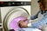 A person is undergoing a medical scan inside an MRI machine, with another individual assisting by adjusting their position. The scene appears clinical, with the MRI machine's interior emitting a soft pink glow. The assistant is wearing a blue checkered shirt and a white apron.