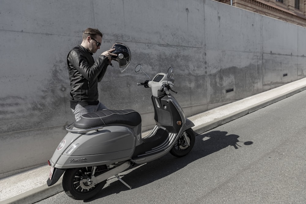 hombre con chaqueta negra montando en scooter gris