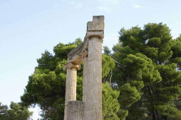 Brown concrete cross with green trees in the background during daytime — Olympia, Greece