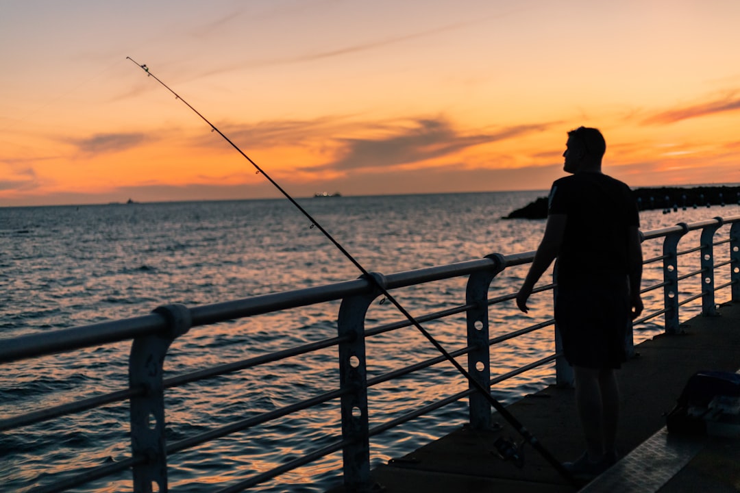 man in black shirt and pants standing on dock during sunset