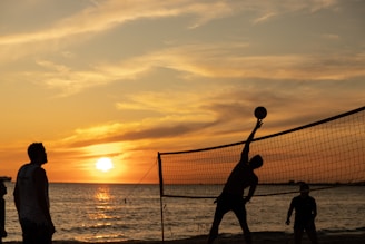 Young athletes playing volleyball passionately on an outdoor court with a vibrant sunset in the background.