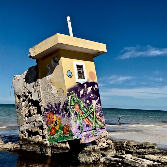 white concrete building on brown rock near sea during daytime in Holbox Mexico