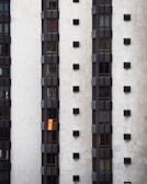 A tall, modern building facade with multiple vertical sections of dark windows is shown. A Spanish flag hangs prominently from one of the windows, adding a splash of color to the otherwise monochromatic scene.
