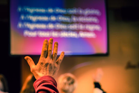 A close-up of hands raised in worship with a blurred cross in the background.