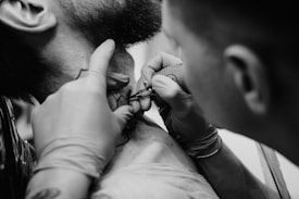 A tattoo artist meticulously inks a man's neck, using a tattoo machine while wearing gloves.