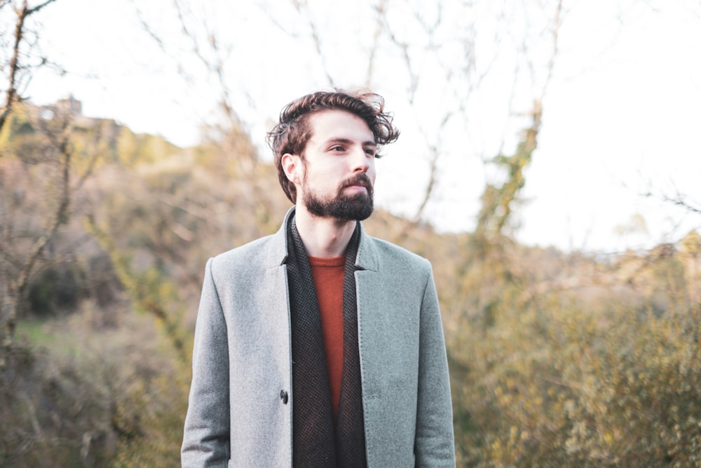 man in gray suit jacket standing near trees during daytime