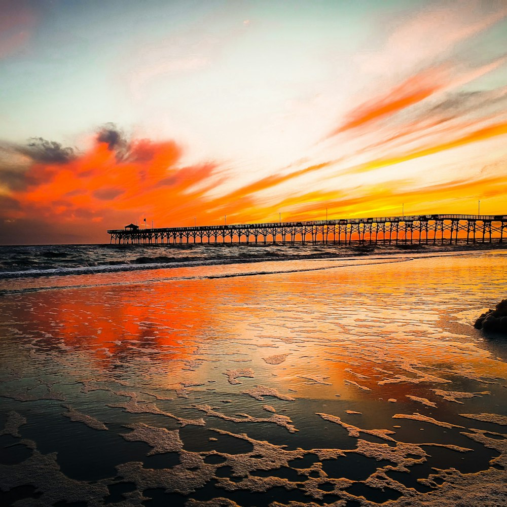 silhouette of dock on body of water during sunset