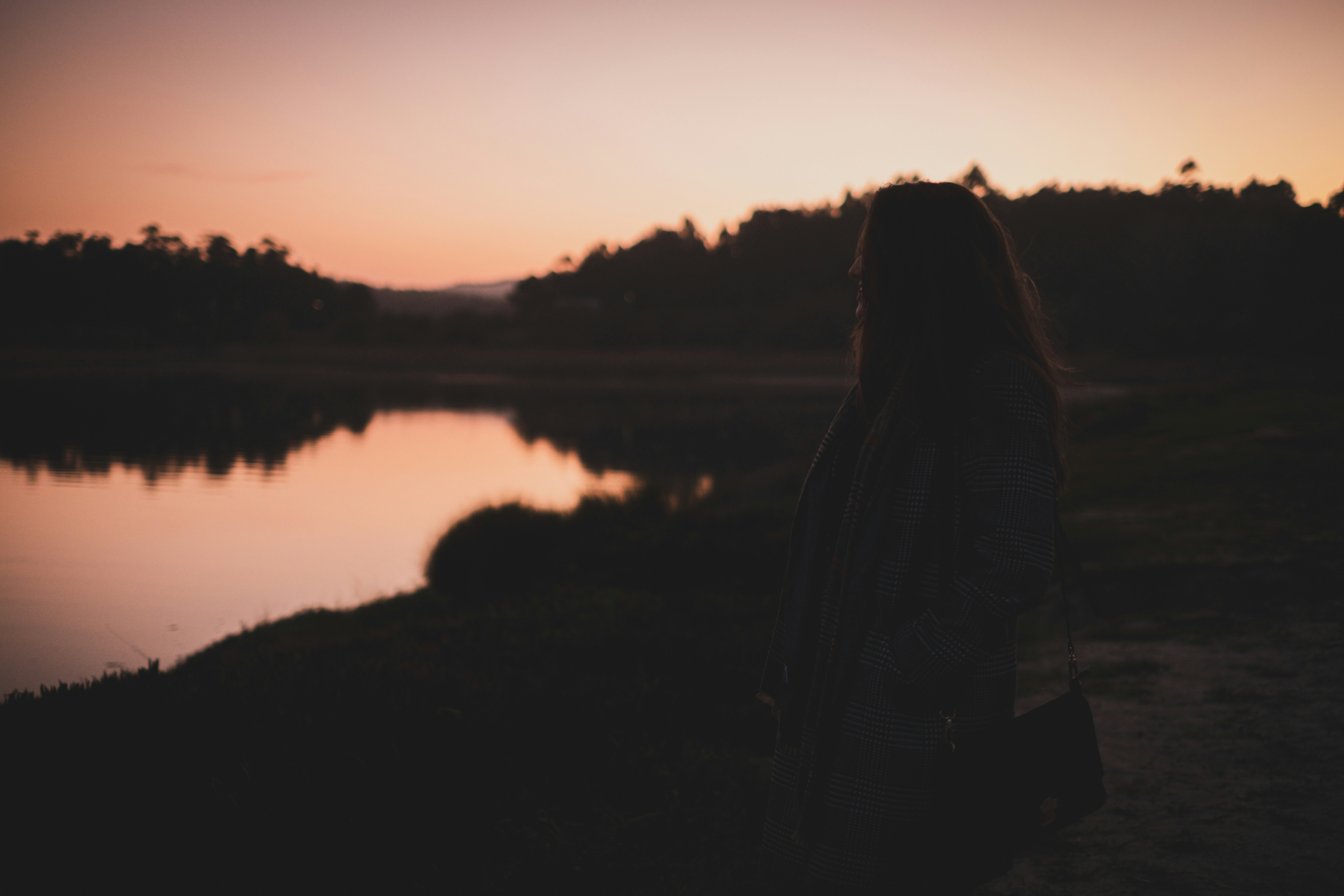woman in black and white plaid dress shirt standing near lake during sunset