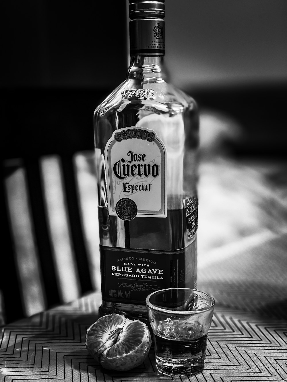 grayscale photo of clear glass bottle beside clear drinking glass