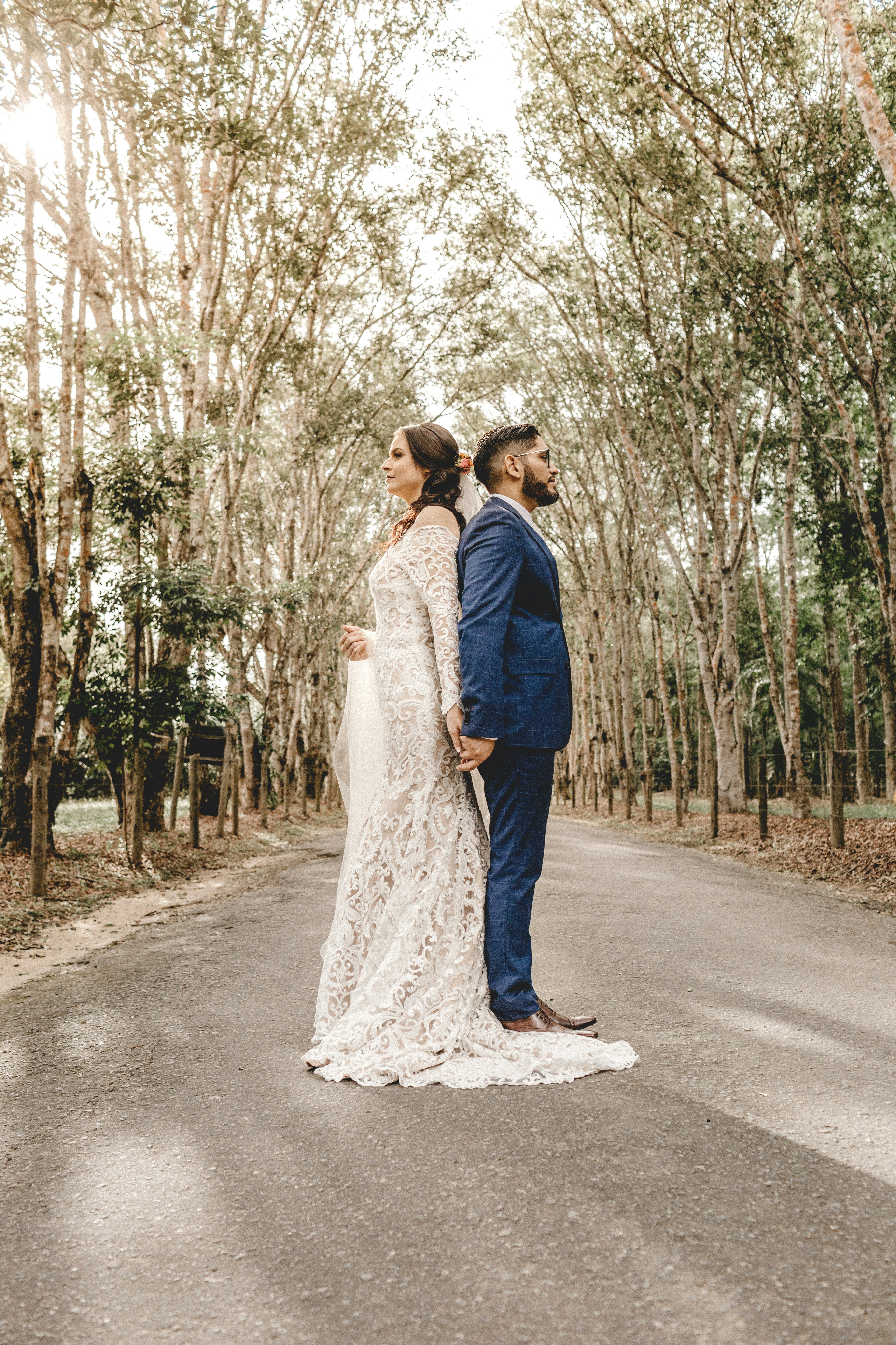 man and woman standing on road between trees during daytime