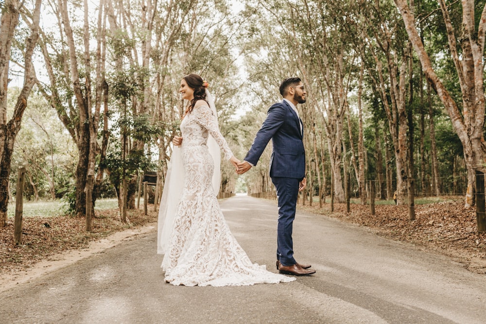 man in black suit jacket and woman in white wedding dress walking on road during daytime