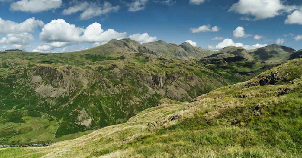 green grass field and mountain under blue sky during daytime