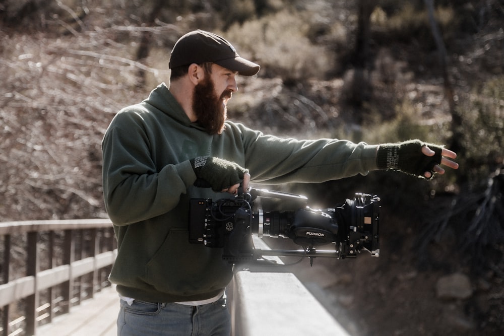 man in green jacket holding black dslr camera