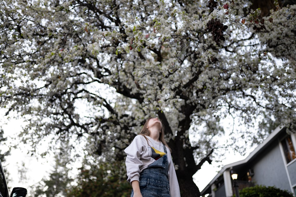 Frau in blauer Jeansjacke und blauen Jeans steht tagsüber in der Nähe von Green Tree