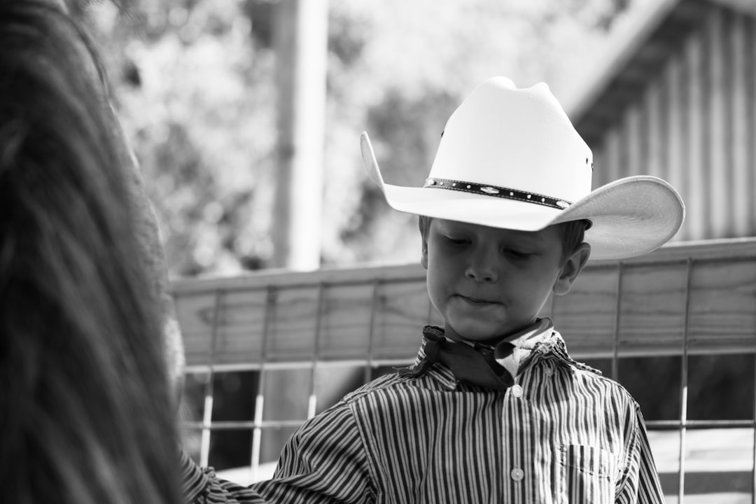 grayscale photo of a boy wearing cowboy hat and striped shirt