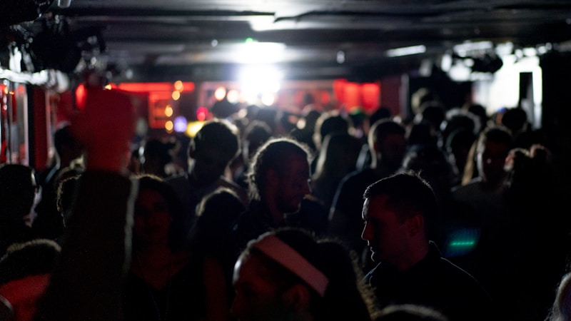 Packed dark venue with low ceiling and crowd silhouettes