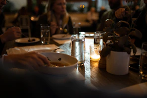 Guests enjoying a lively meal together under soft white lighting, surrounded by green plants